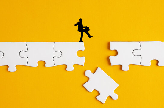 Businessman walking carefully over a bridge made of puzzle pieces about to fall down. Business challenges, risk, hazard and threat concepts.