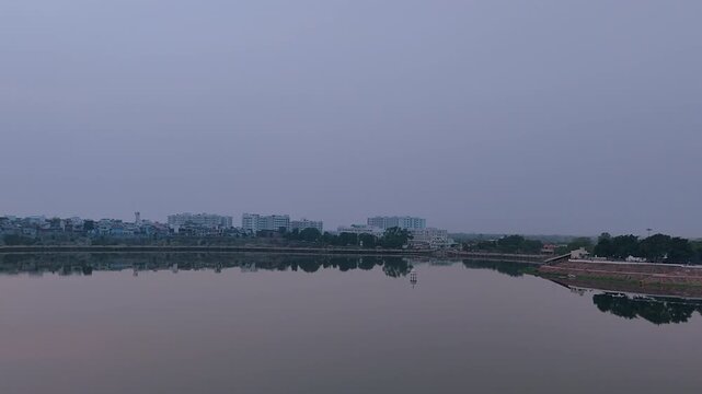 Sharmishtha Lake Vadnagar Gujarat India showing calm water reflection with distant city skyline and soft sky, peaceful urban nature setting ideal for travel, environment and meditation concepts.
