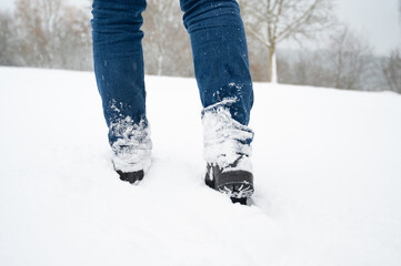 Walking with boots through fresh snow in winter, jeans trousers and shoes covered with snowflakes, frosty, stormy weather conditions in wintertime