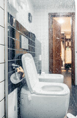 A clean bathroom scene featuring a white toilet and bidet. The glass is fogged, indicating recent use. The setting emphasizes hygiene and care in personal spaces.