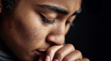 young woman contemplating religion praying with eyes closed deeply feeling sadness grief desperation hope and faith with her hands clasped together in the darkness in a close-up profile