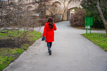 Woman walking in park in Prague during winter without snow wearing red coat. Calm urban walking, everyday lifestyle and seasonal city routine in real life European environment