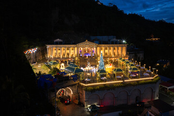 Aerial view of a brightly lit, grand structure with classical columns and festive decorations, standing out against the dark mountain backdrop, Cebu, Cebu City, Philippines.