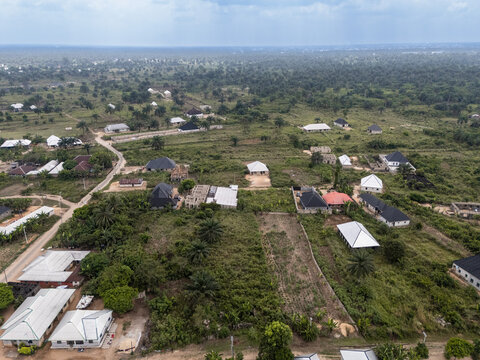 Aerial view of scattered houses and buildings amongst green vegetation, under a soft diffused light, creating a serene yet expansive landscape, Egbema, Rivers, Nigeria.
