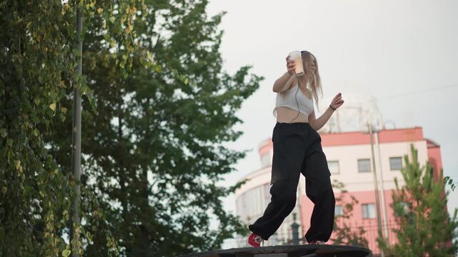 young woman dancing on picnic table, wearing headphones and crop top, braided hair, baggy pants and red sneakers, lively freestyle moves, performer filming with phone, street artist rehearsing