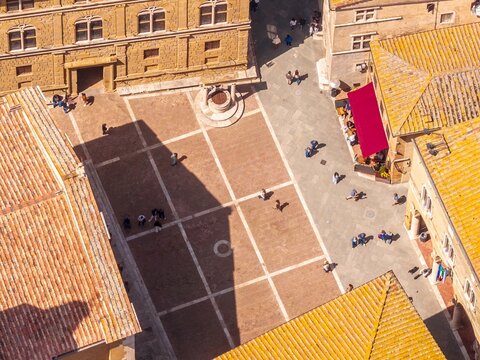 Aerial view of shadows stretching across the Piazza Pio II, the heart of the city, framed by the golden hues of historic buildings, Pienza, Tuscany, Italy.