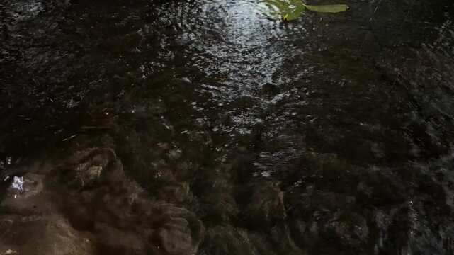 Heavy rain pelting dark paving floor, creating ripples and splashes. 