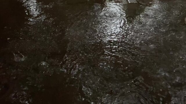 Heavy rain pelting dark paving floor, creating ripples and splashes. 