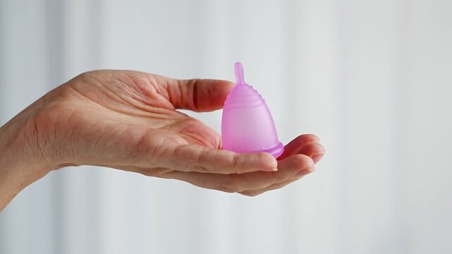 Close-up of a pink menstrual cup standing upright on a woman open palm over wooden table. Feminine hygiene product promoting zero waste, comfort, and sustainable period care.