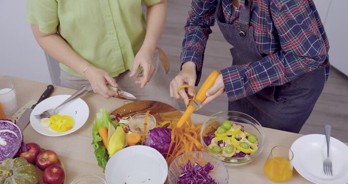 Closeup asian mother and daughter slicing carrots for salad, table filled with fruit and vegetable moment colorful preparation, teamwork, homemade meal, retirement leisure, family wellness lifestyle