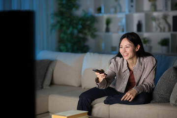 Happy asian woman using remote watching tv in the night