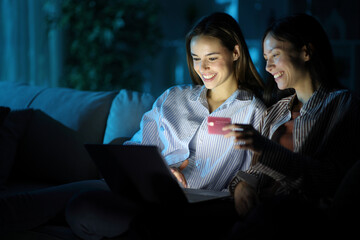 Happy friends paying online in the night at home