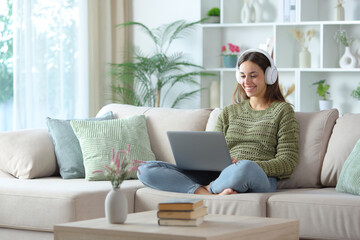 Happy woman in green wearing headphone checking laptop