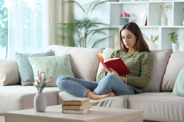 Relaxed woman in green reading red paper book at home