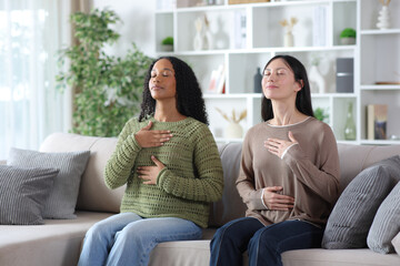 Two diverse friends doing breathing exercises at home