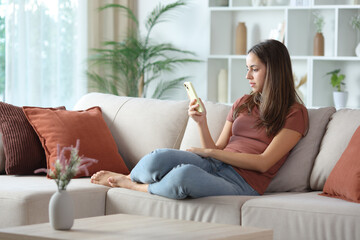 Serious woman at home checking cell phone on a sofa