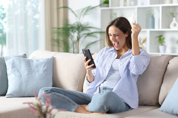 Excited woman in blue checking smart phone on a sofa