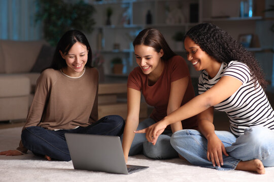 Three diverse friends checking laptop content in the night at home