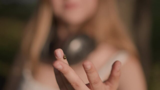 outdoor young woman with headphones and ladybug on fingertip, playful sunlit sequence showing dancer enjoying music, expressive hand gestures, soft skin tones and warm bokeh, candid park scene