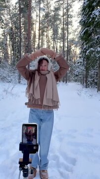 Teenage girl recording a vertical dance video in a snowy winter forest. Social media content creation, youth culture, self expression and dancing in nature.