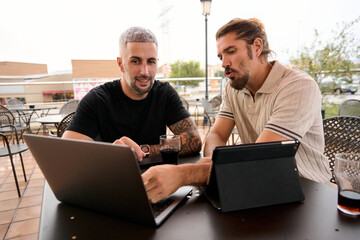 Friends collaborating on laptop and tablet outdoors