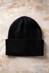 Black knitted beanie laid on a textured surface showcasing its simple design for cold weather wear