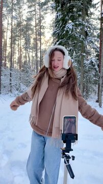 Teenage girl recording a vertical dance video in a snowy winter forest. Social media content creation, youth culture, self expression and dancing in nature.