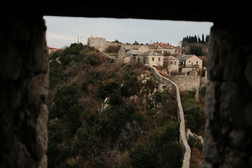Ancient stone wall of Pocitelj Fortress leading toward historic houses on a hilltop, surrounded by...