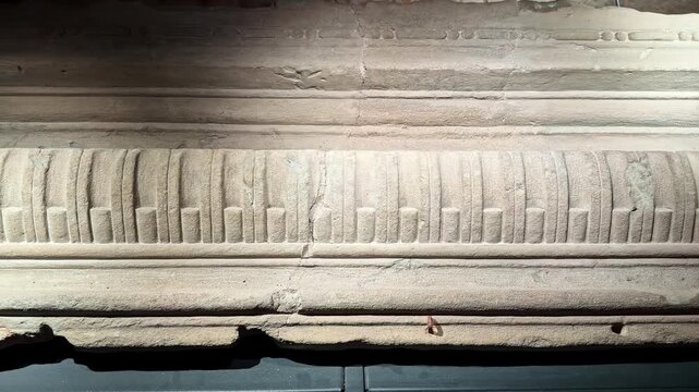 Close-up of carved limestone frieze and cornice molding in a museum display, showing medieval decorative stonework, chisel marks, and weathered surface detail.