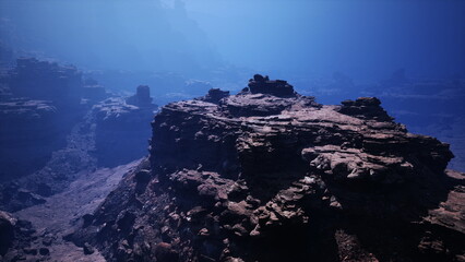Venture into a deep underwater scene showcasing rugged rock formations illuminated by faint blue...