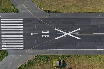 Aerial view of the stark black runway marked with bright white lines and bold numbers, contrasted against the surrounding green grass at Flughafen Tegel, Berlin, Berlin, Germany.