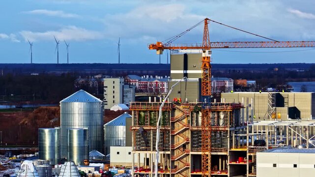 Data center complex under construction showing modular buildings and surrounding suburban infrastructure with wind turbines in backdrop, aerial establish