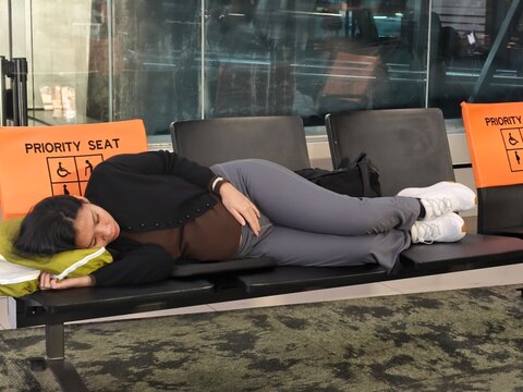 A pregnant woman lying on priority seating in an airport waiting area, resting during travel while waiting for a flight