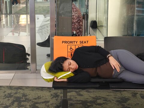 Pregnant woman lying down and resting on priority seating in an airport terminal while waiting for her flight, highlighting travel fatigue and maternity care
