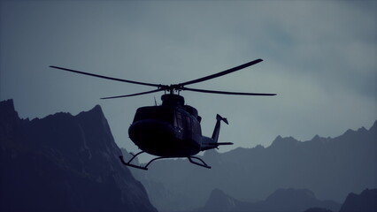 A helicopter hovers amid jagged mountain peaks under an overcast sky at dusk. The scene captures a moment of adventure and exploration in a remote area filled with natural beauty. © icetray