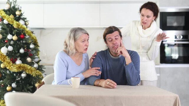 Senior woman sits near man and comforts him during quarrel with wife on Christmas Eve. Mother calms upset son takes his side in altercation with girlfriend. Woman is outraged by man behavior 