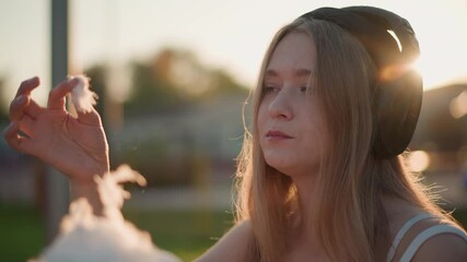 sunset fairground white teen headphones enjoying cotton candy with gentle smile, golden rim light, soft backlight portrait, casual student vibe, aspiring musician gesture, street performer observer,