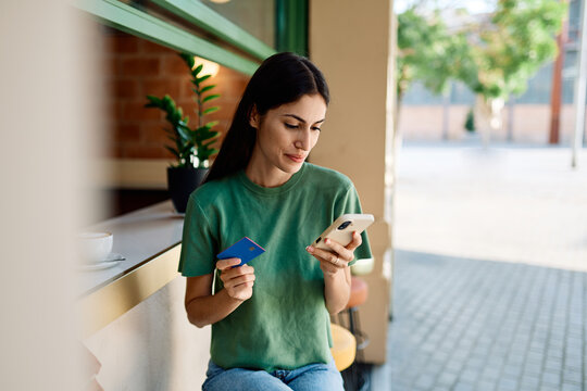 Young woman using credit card for online shopping on her phone drinking coffee in caffee cafeteria