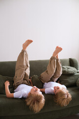 Two boys having fun, lying upside down on the couch, laughing