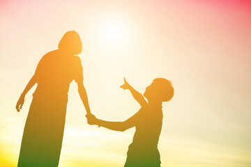 Mother encouraged her son outdoors at sunset, silhouette concept

