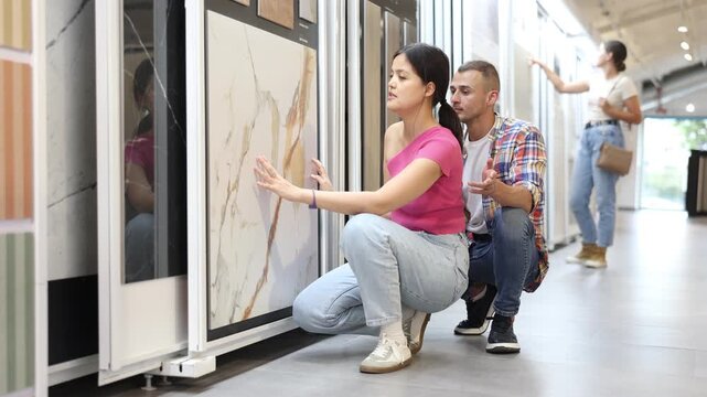  Couple of young man and woman customers selecting tiles from samples in hardware store