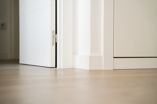 Low angle view of white interior door opening onto light wooden floor, minimalist apartment detail with baseboards and clean modern design