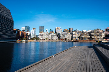 Daylight on blue urban waterfront boardwalk beside harbor with city skyline showing modern architecture and soft reflection on calm water