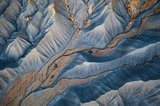 Aerial view of layered rock formations and winding washes create a tapestry of cool blues and warm browns, Hanksville, Utah, United States.
