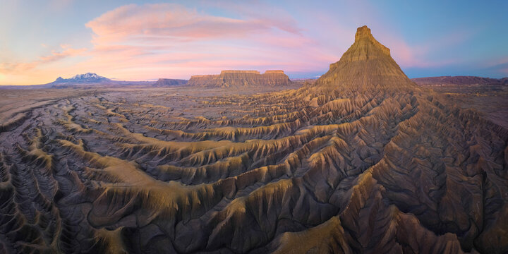 Aerial view of stark, eroded badlands bathed in the warm glow of sunset, with Factory Butte rising majestically against the pastel sky, Hanksville, Utah, United States.