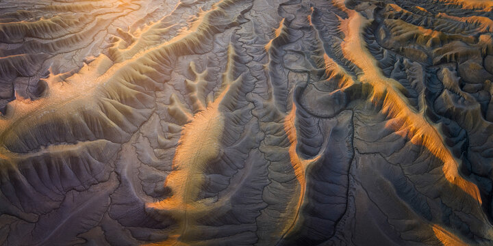 Aerial view of stark badlands carved by time and light, where shadows dance with the terrain's rugged textures, Hanksville, Utah, United States.