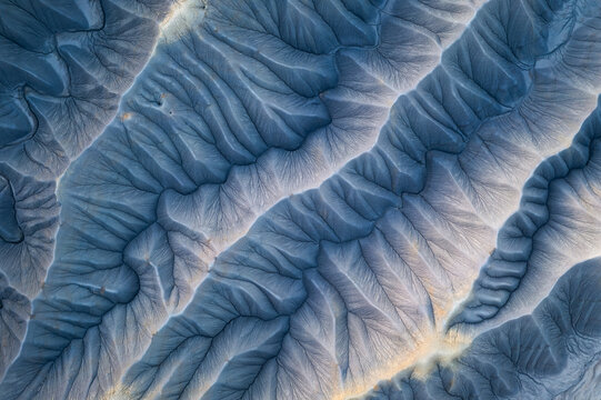 Aerial view of the earth's surface reveals a stunning tapestry of blue and beige, sculpted by time and the elements into an intricate network of ridges and valleys, Hanksville, Utah, United States.