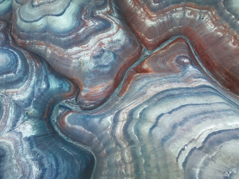 Aerial view of swirling, banded rock formations in shades of blue, purple, and brown create an otherworldly landscape, Hanksville, Utah, United States.
