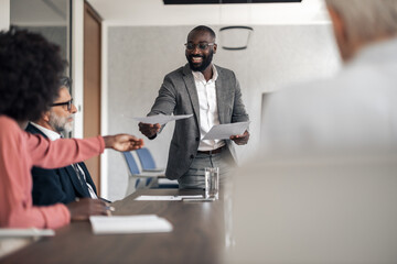 Black executive delivering documents during business meeting presentation