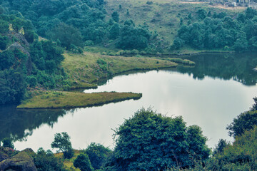 Obraz premium View of a calm lake surrounded by green hills and trees in the afternoon light showing nature in a rural area